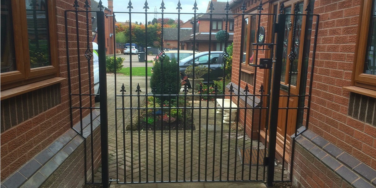 A wide single gate with fleur de lys finials and a security lock