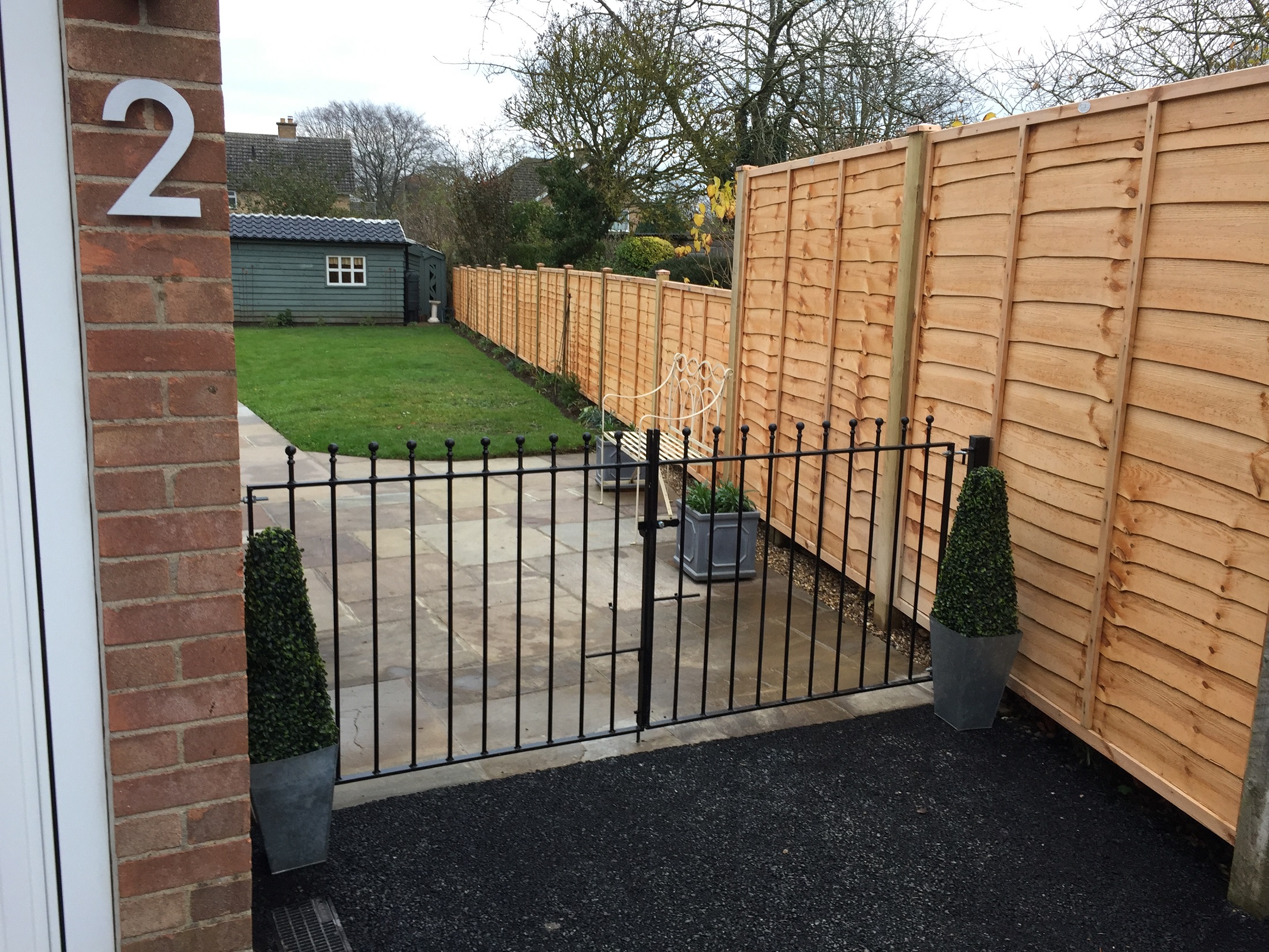 Manor metal driveway gates fitted between house wall and wooden fence panels