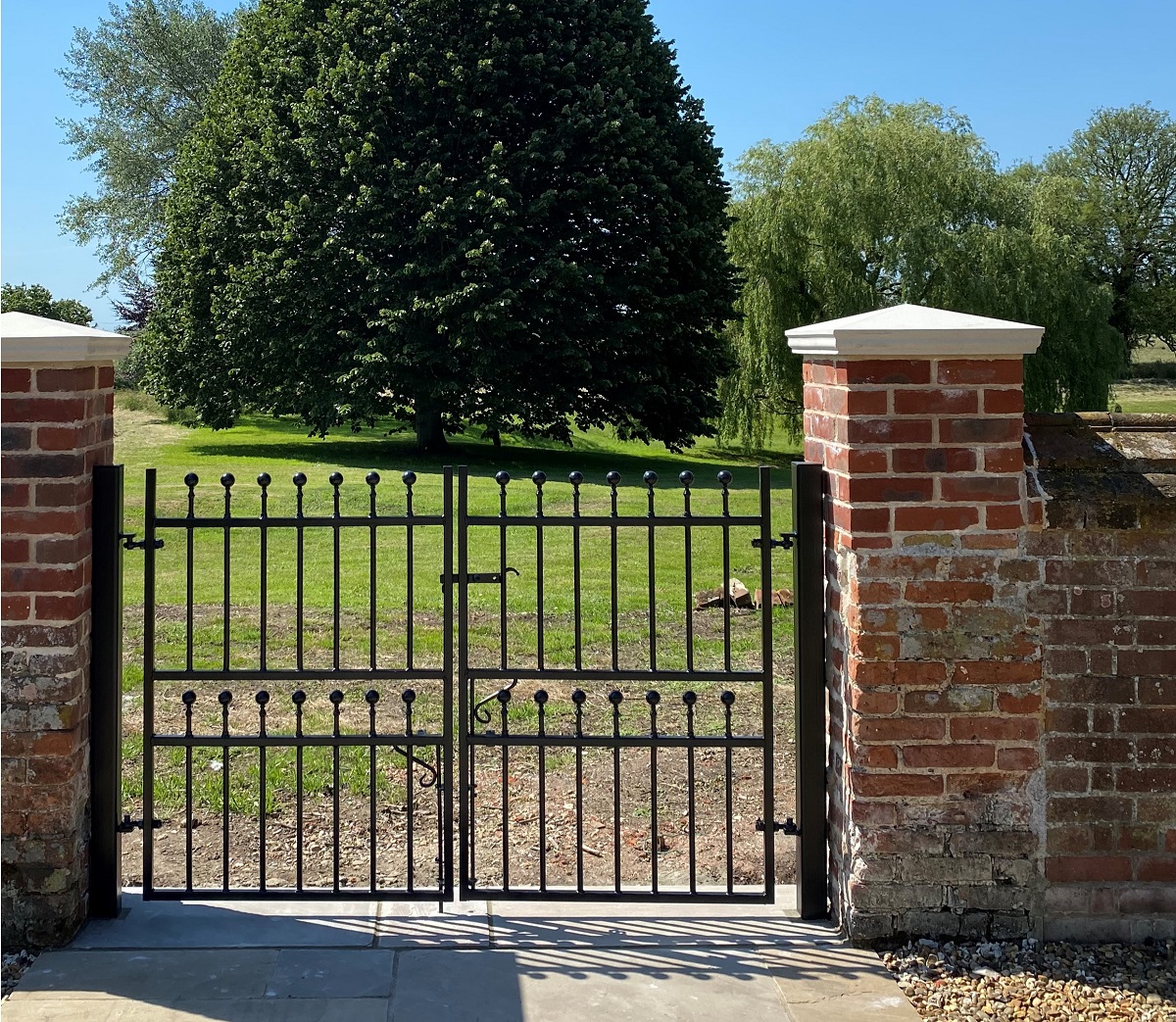 Small bespoke double gates with vertical bars and ball top finial in a narrow entrance